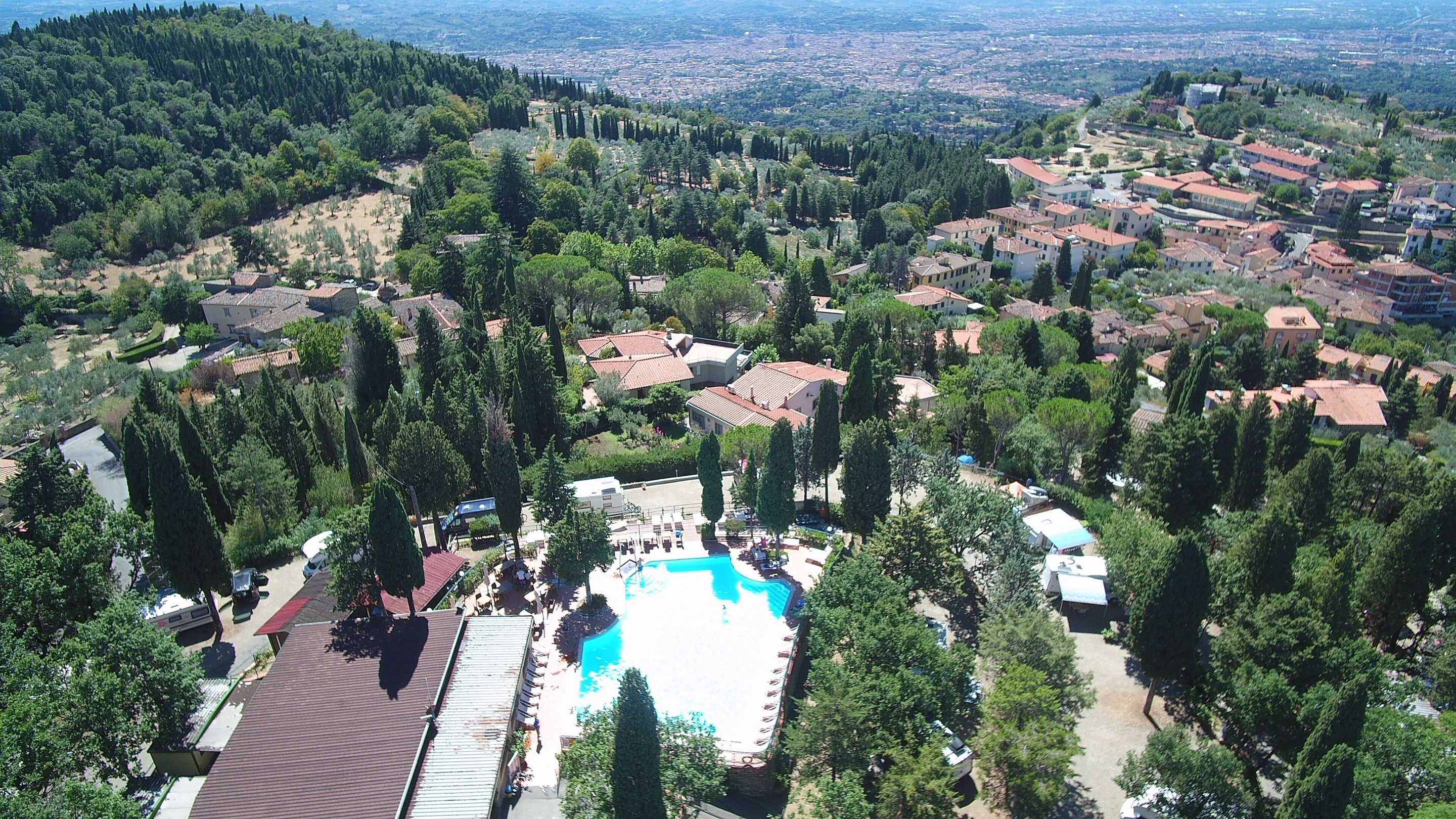 Vue aérienne d’un quartier résidentiel avec une piscine entourée d’arbres et de maisons.
