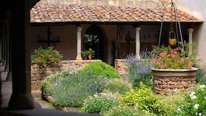 Un patio con techo de tejas, paredes de piedra y varios maceteros con plantas y flores.
