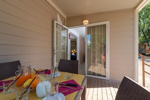 A table set with a pitcher, glasses, and fruit on a deck with a view of a building through a glass door.