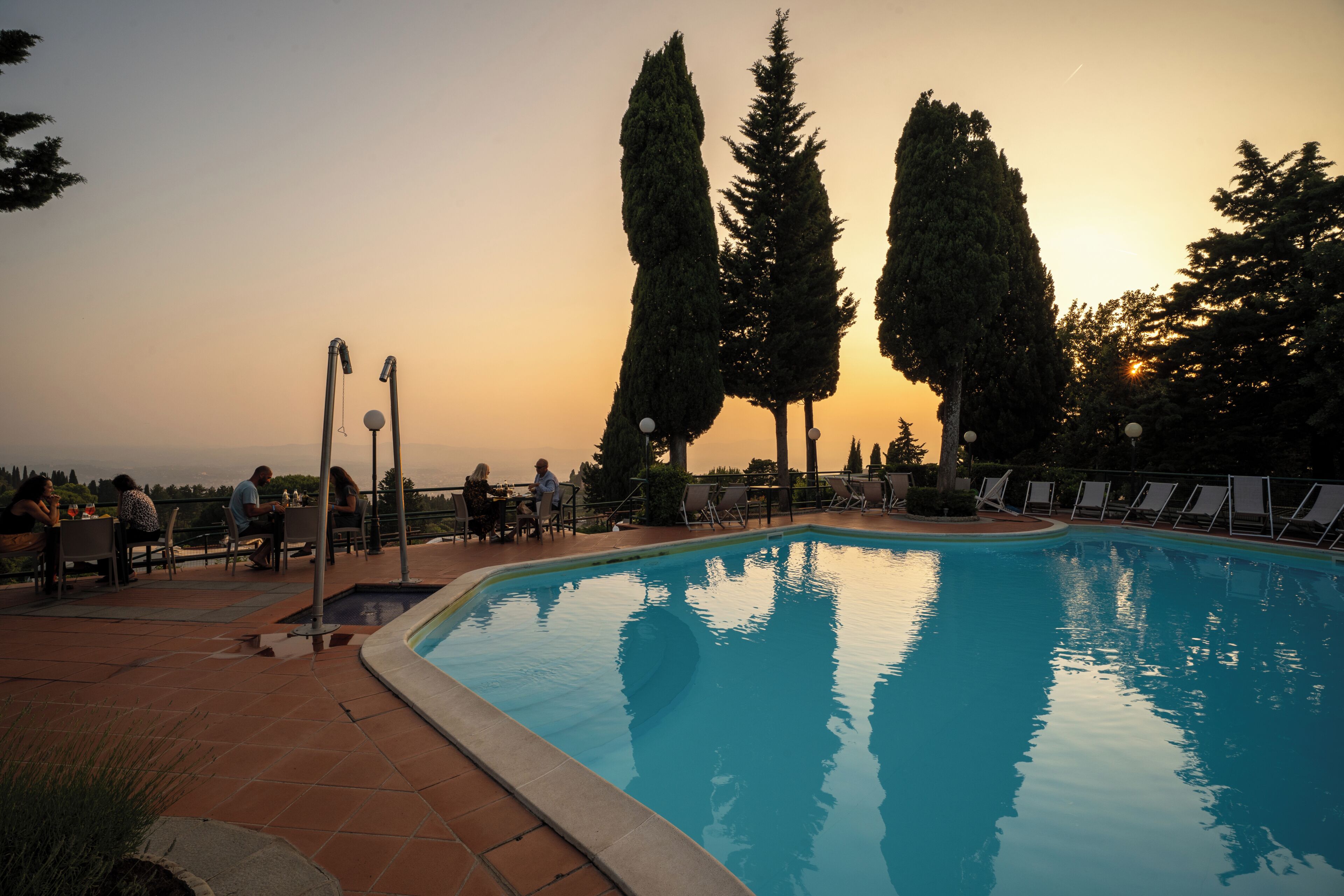 Una piscina con sdraio e alberi alti sullo sfondo.