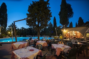 Un espace extérieur aménagé pour les repas, avec des tables pour deux personnes, donnant sur une piscine.
