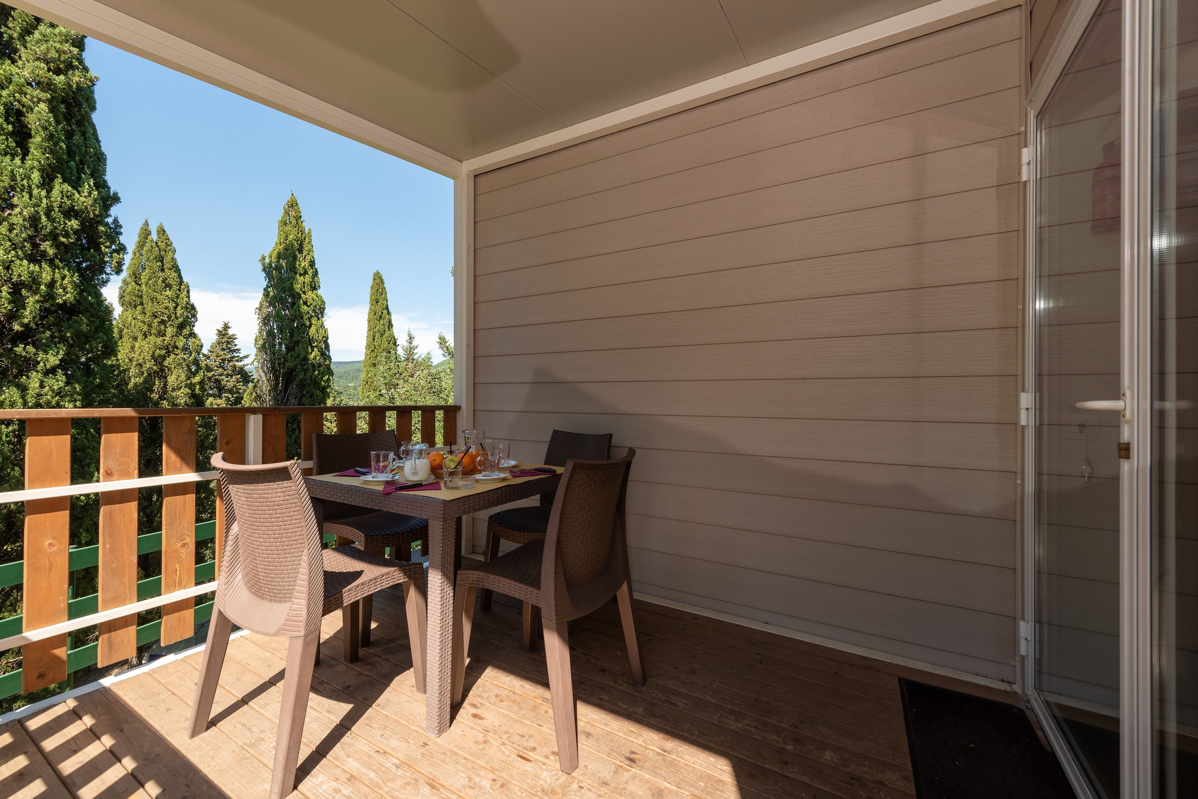 Una veranda riparata con tavolo e sedie, un pontile in legno e vista sugli alberi.