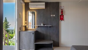 Un baño moderno con lavamanos empotrado, un espejo y un estante. Hay un extintor de incendios montado en la pared y una ventana que ofrece vistas a la vegetación exterior.