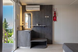 Un baño moderno con lavamanos empotrado, un espejo y un estante. Hay un extintor de incendios montado en la pared y una ventana que ofrece vistas a la vegetación exterior.