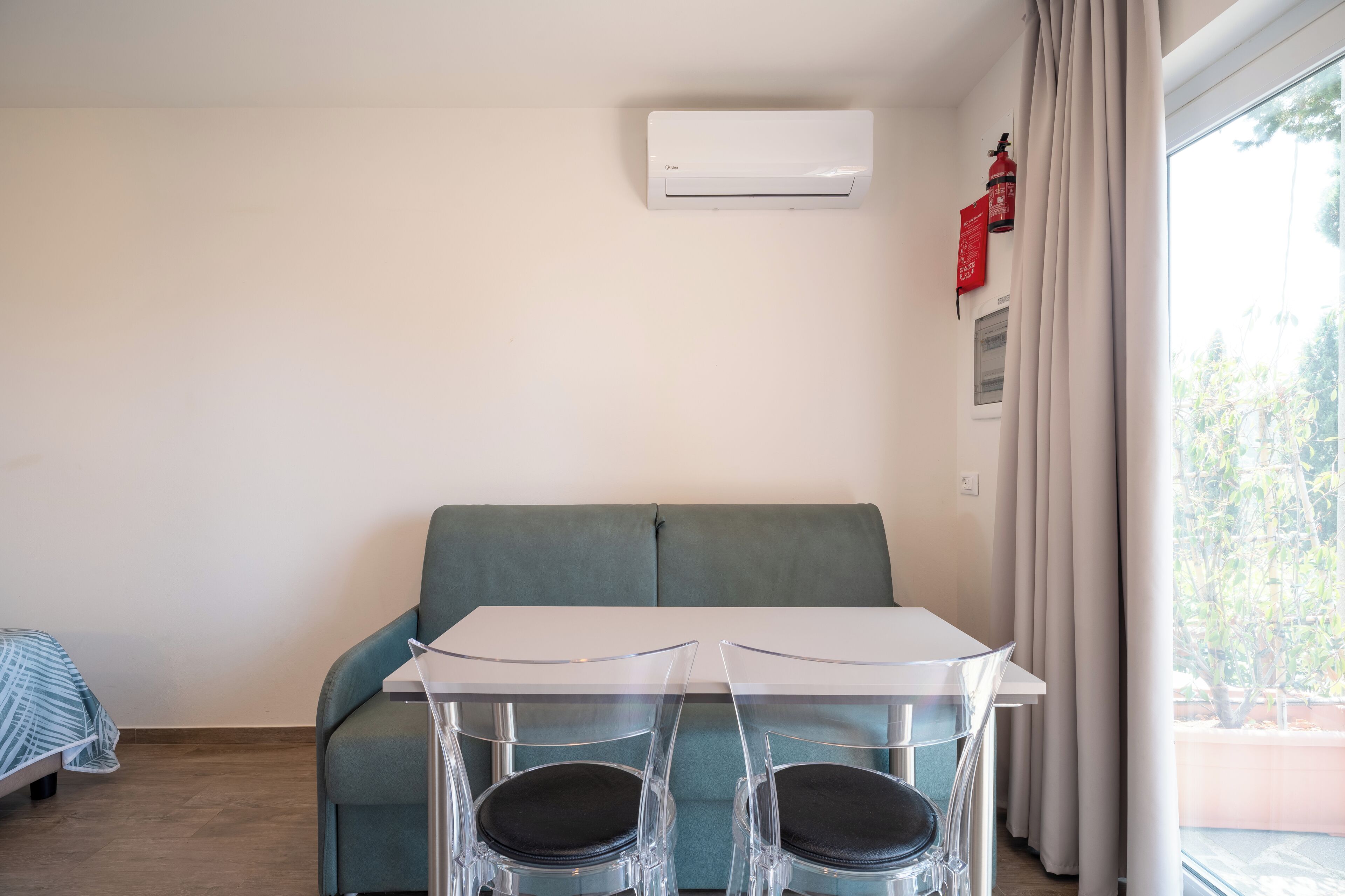 Una stanza moderna e accogliente con un tavolo bianco, due sedie trasparenti, un divano verde e una finestra con tende.