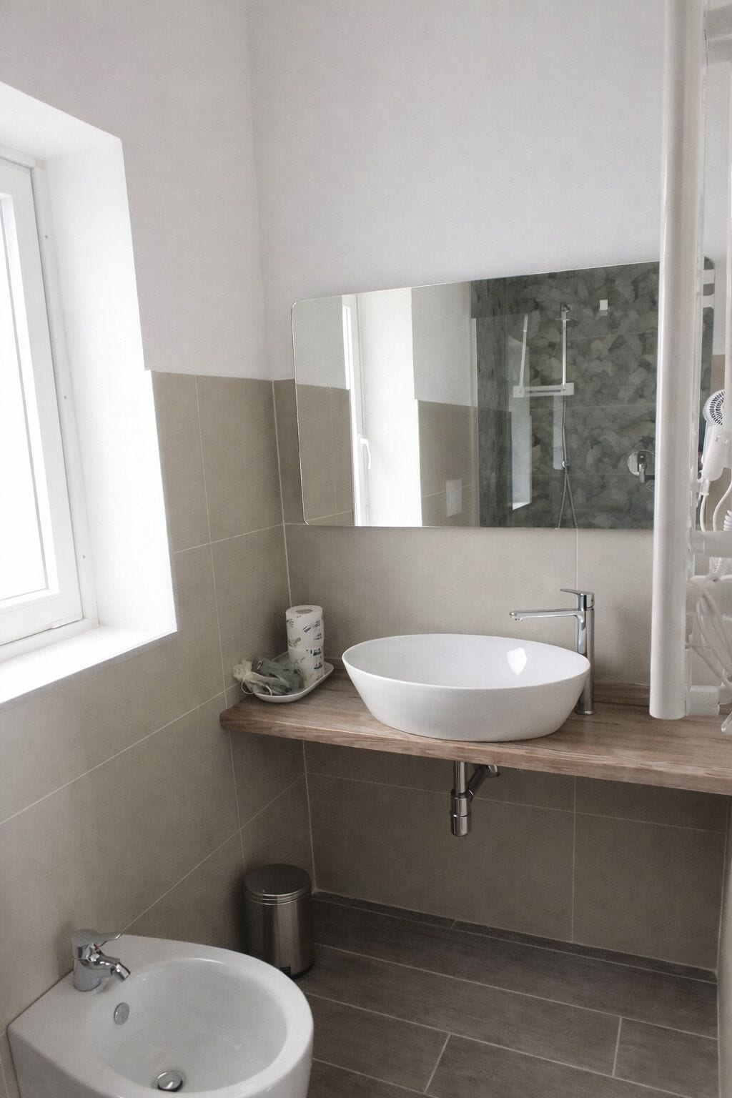 Een badkamer met een groot wit wastafel, een spiegel, een raam en een douchehoek.