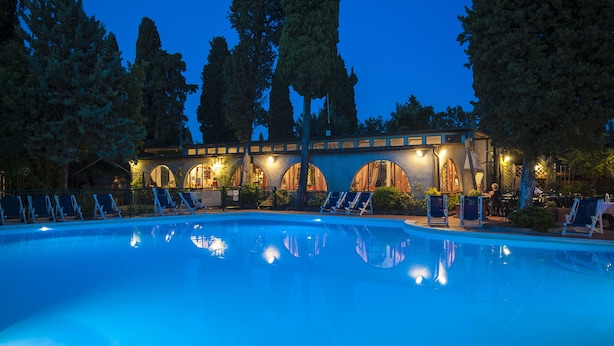 Una piscina con sillas de descanso y un edificio con ventanas arqueadas al fondo.