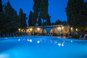 Una piscina con sillas de descanso y un edificio con ventanas arqueadas al fondo.