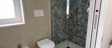 Un baño con bidé, inodoro y ducha con mampara de vidrio.