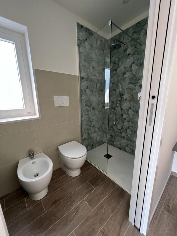 A bathroom with a bidet, toilet, and glass-enclosed shower.