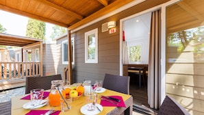 Un espacio de comedor al aire libre cubierto, con una mesa preparada para dos personas, que incluye una silla de mimbre, una mesa de madera y una jarra de vidrio con jugo de naranja.