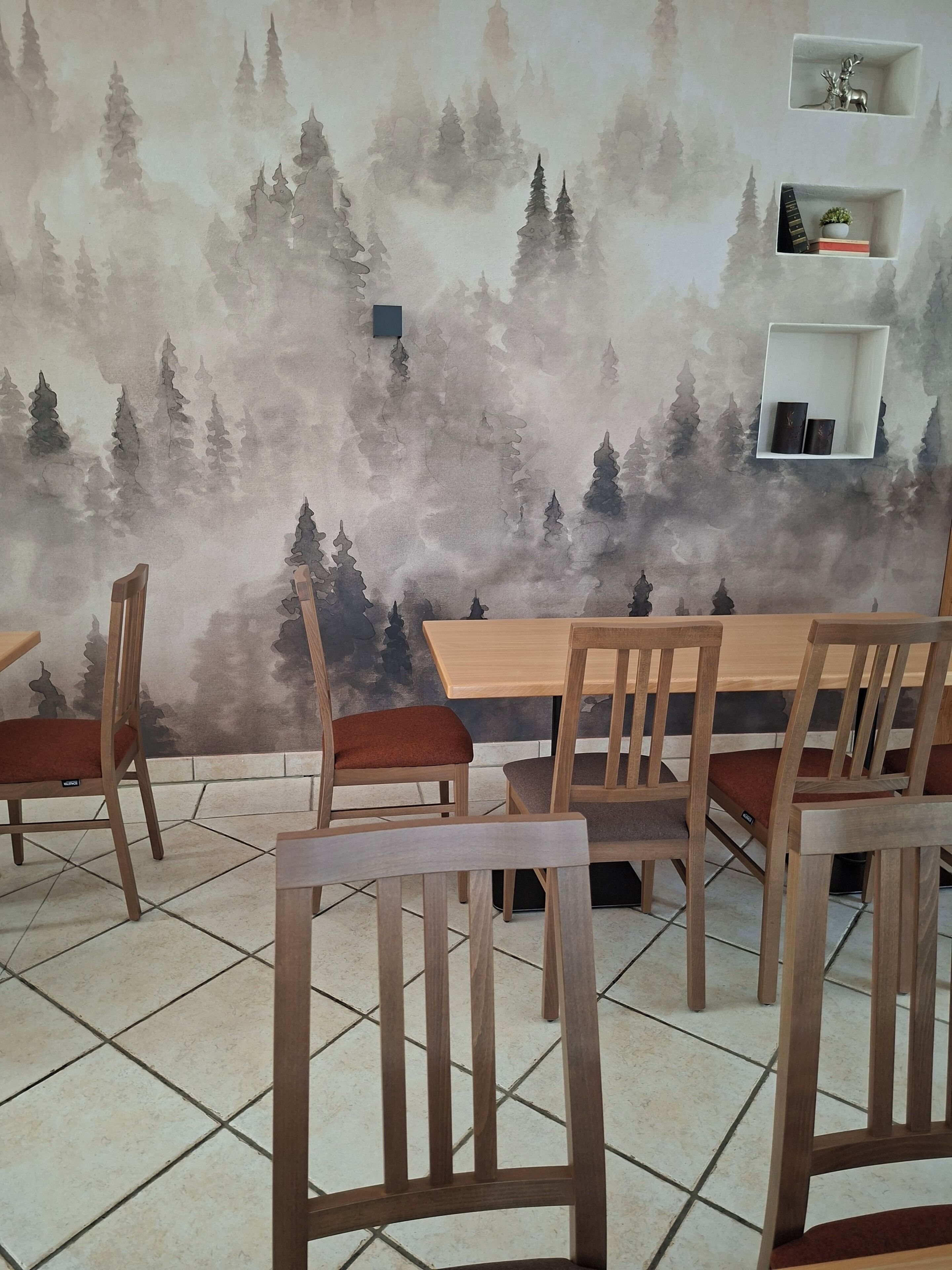 Un comedor con un mural de un paisaje boscoso, sillas y una mesa de madera, y estantes en la pared con adornos.
