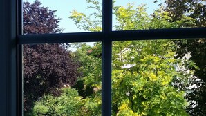 A window with a view of a garden with various trees and a stone pathway. - Wirth z Moosham (Kirchdorf)