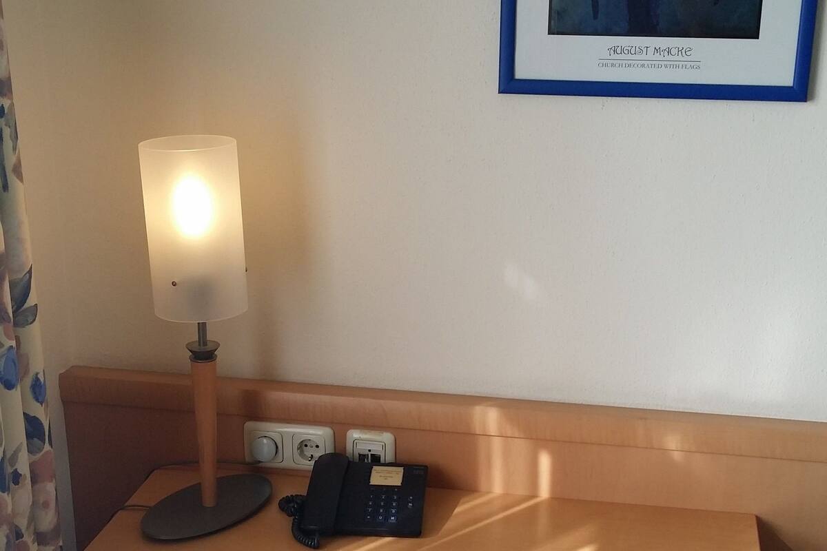 Ein Hotelzimmer mit einem Holztisch, einer Lampe, einem Telefon und einem gerahmten Bild an der Wand.