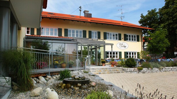 A building with a glass entrance, outdoor seating, and a stone pathway. - Wirth z Moosham (Kirchdorf)