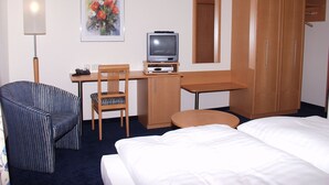 A hotel room with a bed, a desk with a television, a chair, a wardrobe, and a painting on the wall. - Wirth z Moosham (Kirchdorf)