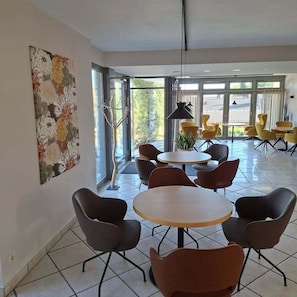 A modern interior with round tables and chairs, large windows, and a decorative wall piece. - Wirth z Moosham (Kirchdorf)