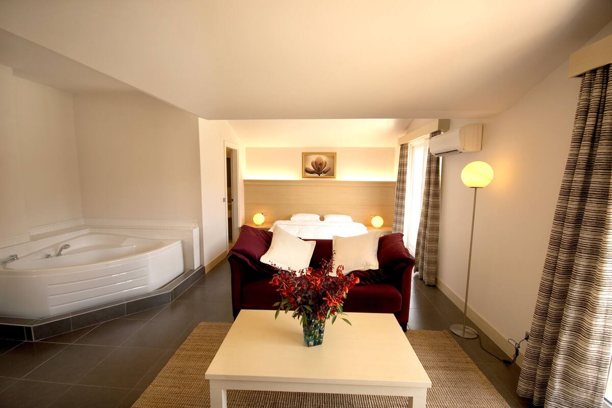 Ein Hotelzimmer mit einer großen Badewanne, einem Sofa mit Tisch und einer Blumenvase.