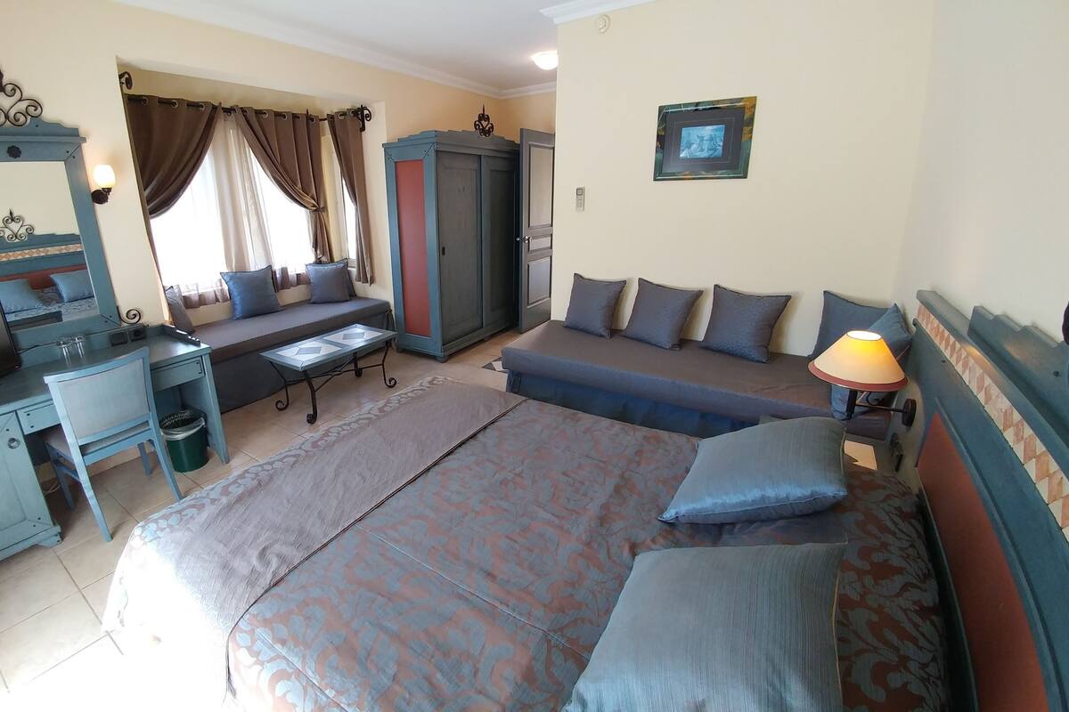 Ein Hotelzimmer mit Bett, Schreibtisch, Fernseher, Sofa und Kleiderschrank.