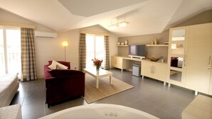 Una sala de estar moderna con un sofá rojo, una mesa de centro blanca, un televisor y una zona de cocina con armarios y un refrigerador.