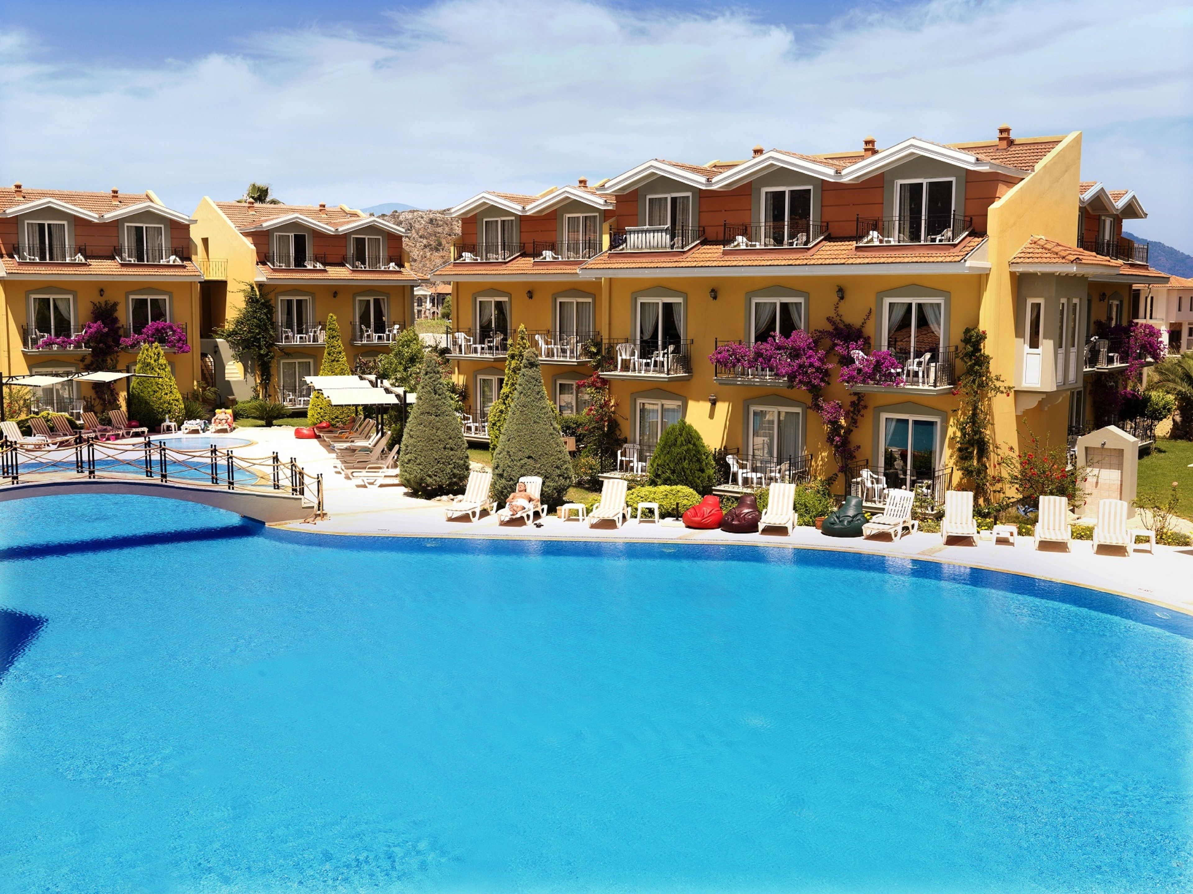 Un hotel con piscina, varios balcones y zonas de estar al aire libre.