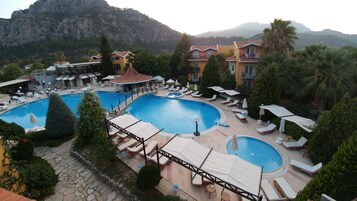 Un resort con varias piscinas, zonas de descanso y montañas al fondo.