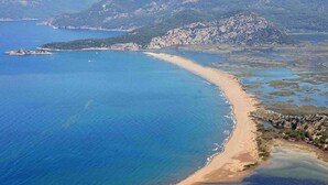Vista aérea de una zona costera con playa arenosa, aguas azules cristalinas y colinas circundantes.
