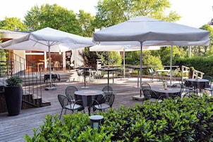 Area patio esterna con tavoli e sedie, riparata da ombrelloni, circondata da vegetazione.