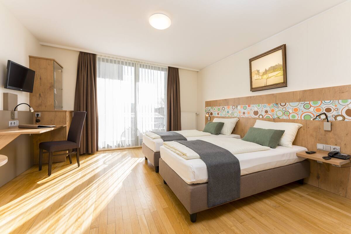 Een hotelkamer met twee bedden, een bureau, een stoel, een televisie en een raam met gordijnen.