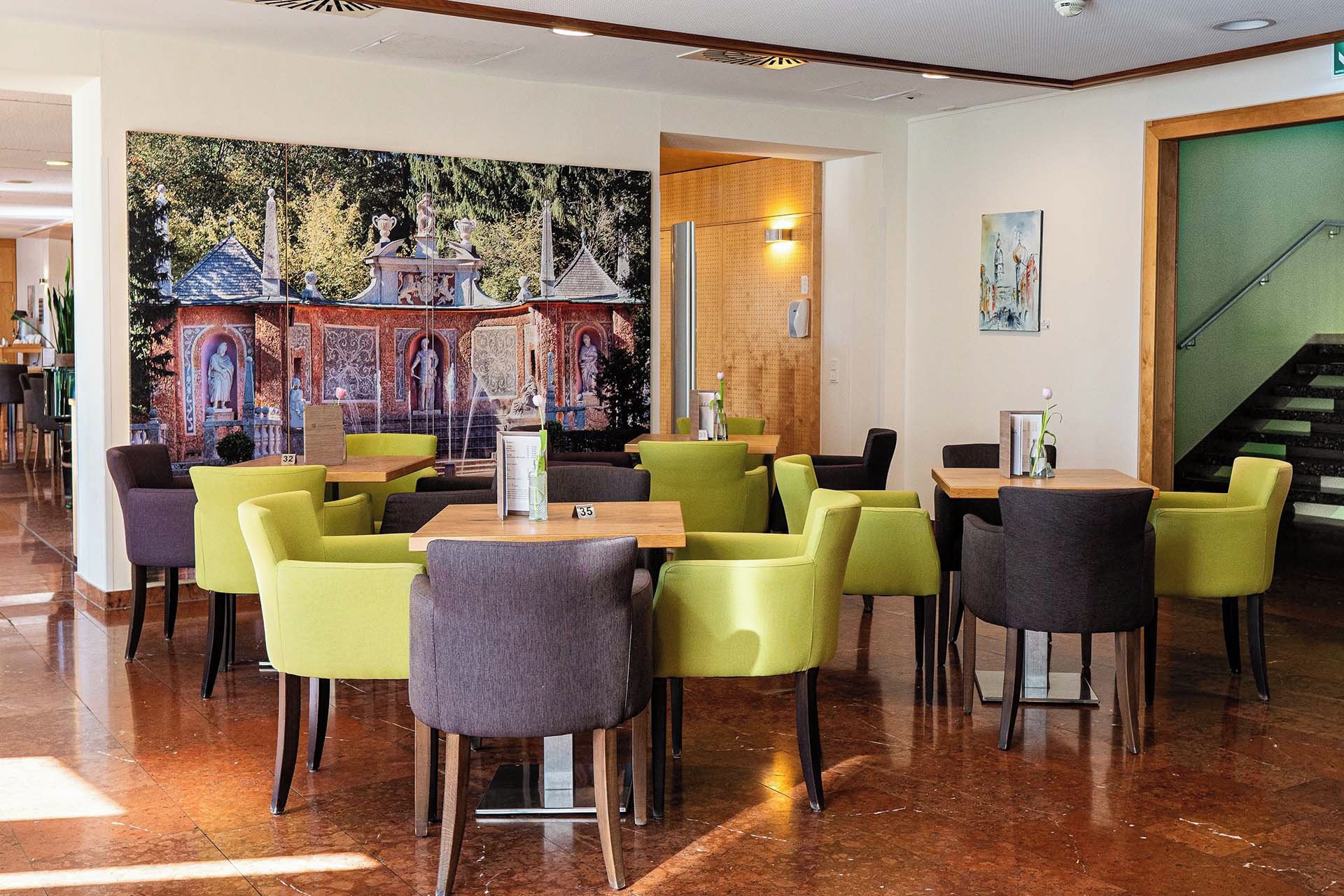 A restaurant with a mural of a castle, green and gray chairs, and a wooden table.