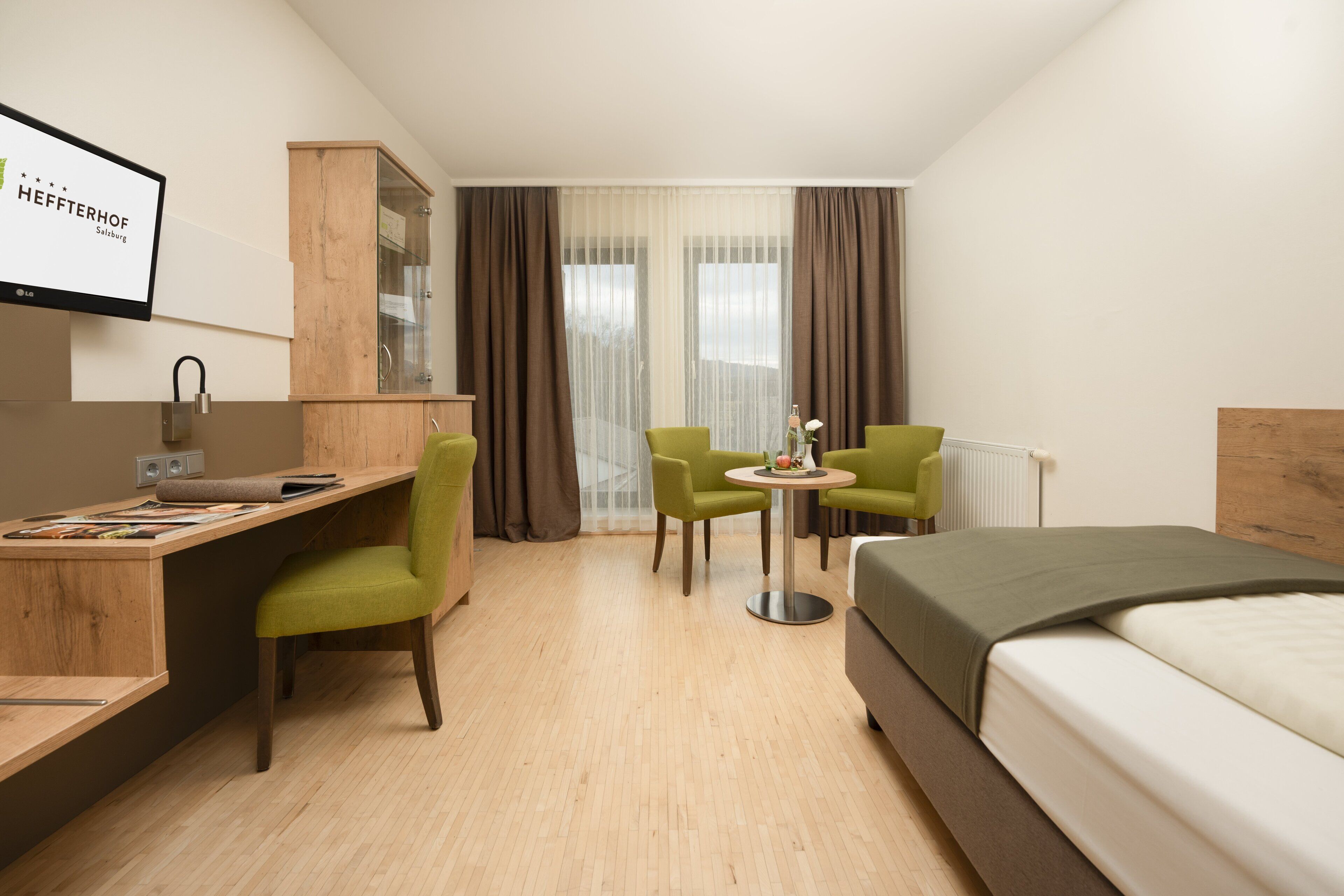 A hotel room with a bed, a desk with a computer, two chairs, a small table, and a cabinet.