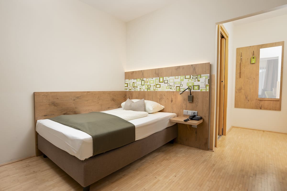 Een moderne slaapkamer met een houten hoofdbord, een bed met wit en groen beddengoed, een nachtkastje met een lamp en een raam met gordijnen.