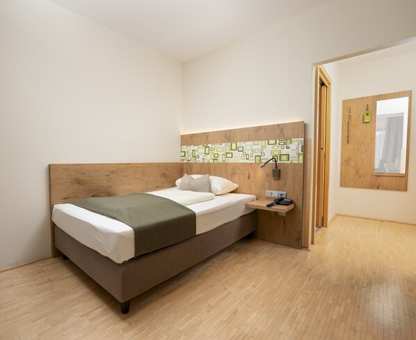 Un dormitorio moderno con cabecera de madera, cama con ropa de cama blanca y verde, mesita de noche con lámpara y ventana con cortinas.