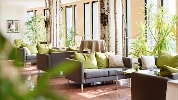 Ein modernes Wohnzimmer mit einer Sofagarnitur, einem Couchtisch und großen Fenstern mit vertikalen Jalousien.