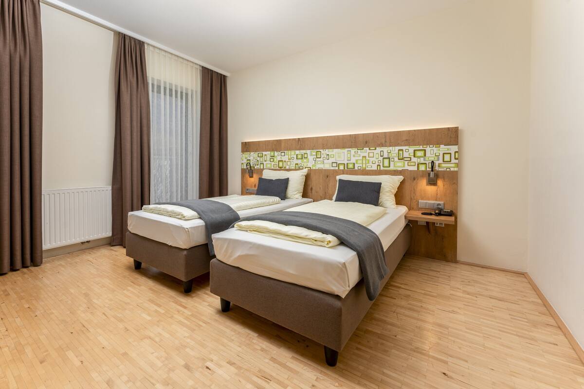 Een tweepersoonsbed met een houten hoofdeinde, twee nachtkastjes en een raam met gordijnen.