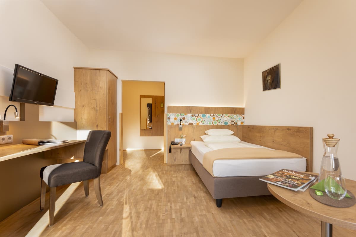 Een hotelkamer met een bed, een bureau met stoel, een televisie en een nachtkastje met lamp.
