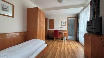 A hotel room with a single bed, a desk with a chair, a television, and a wardrobe.