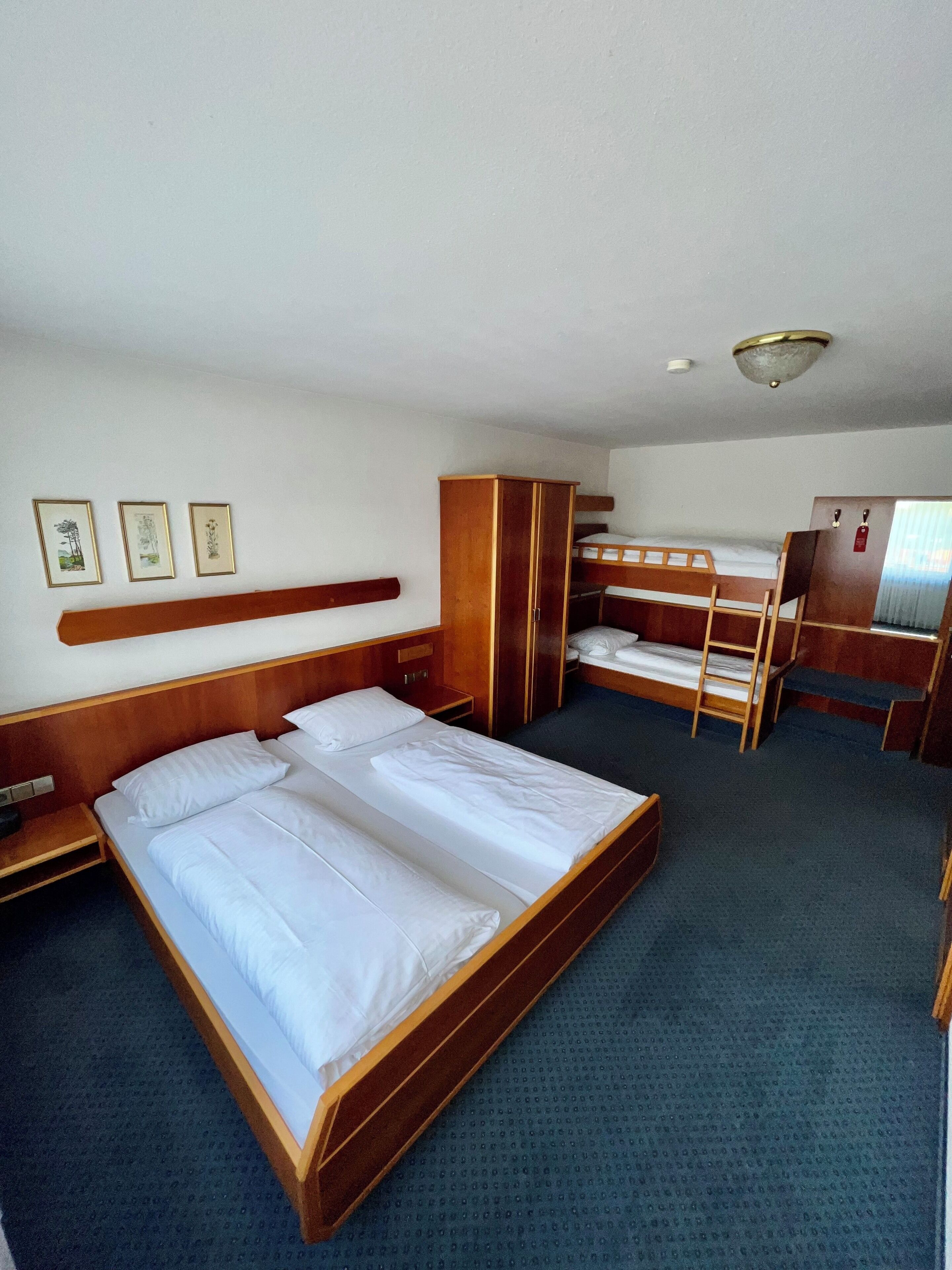 Habitación de hotel con una cama grande, una cama más pequeña, un armario, un escritorio y una litera.