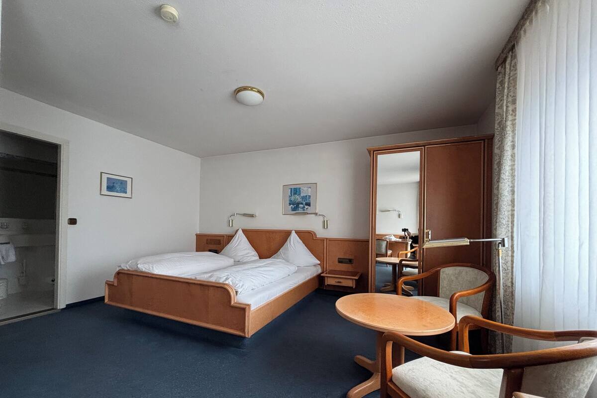 Ein Hotelzimmer mit Bett, einem kleinen Tisch, einem Sessel, einem Spiegel und einem Kleiderschrank.