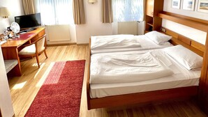 A hotel room with a wooden bed, a desk with a computer, a TV, and a red rug. - Hotel Krone Neuenburg (Neuenburg am Rhein)
