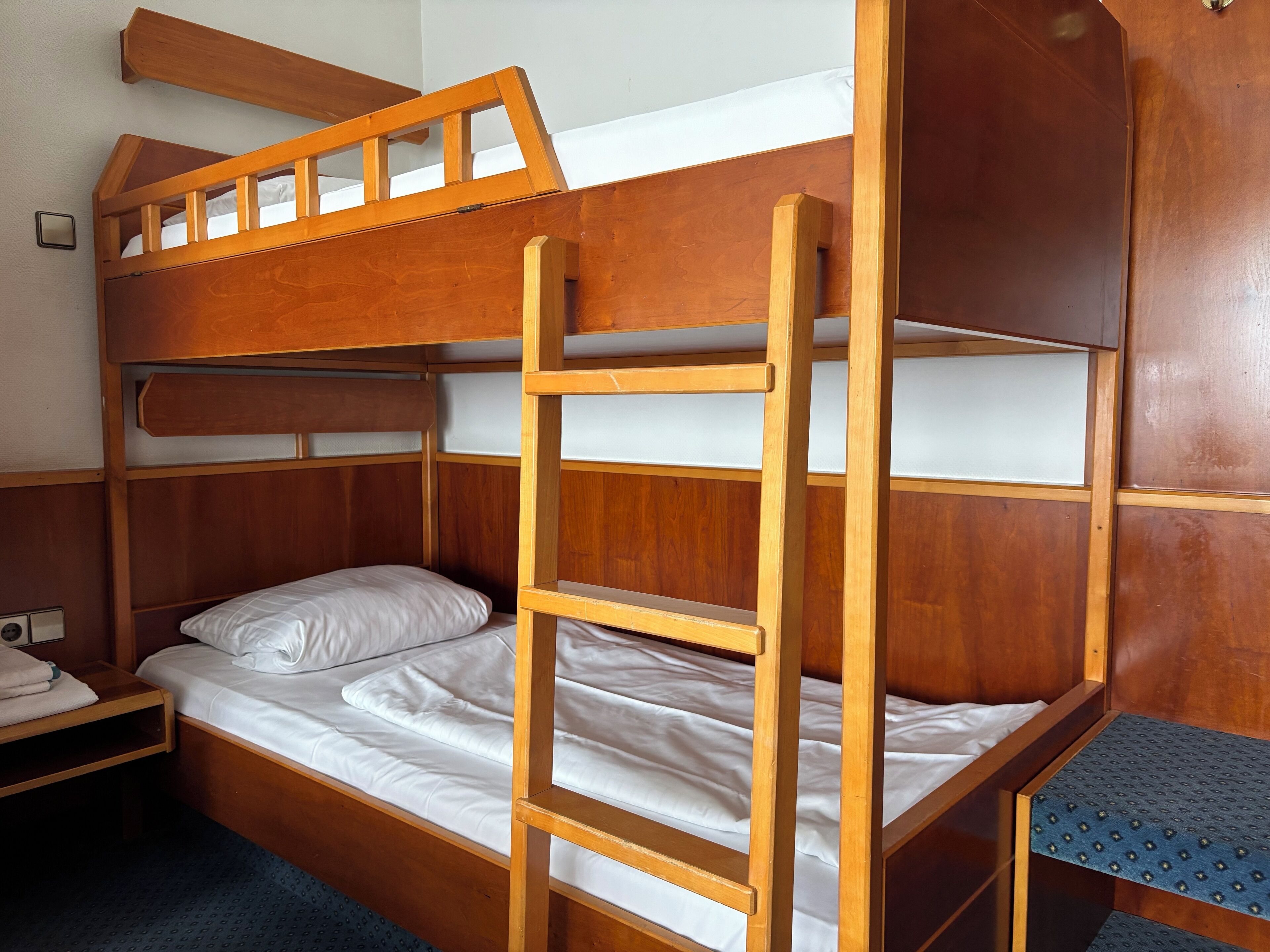 A bunk bed with a ladder, a bedside table, and a small shelf.