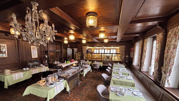 A restaurant with a rustic interior, featuring wooden beams, a large chandelier, and a long counter with a buffet. - Hotel Krone Neuenburg (Neuenburg am Rhein)