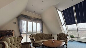 A spacious room with a high ceiling, a large window with curtains, and a round wooden table with a vase. - Hotel Krone Neuenburg (Neuenburg am Rhein)