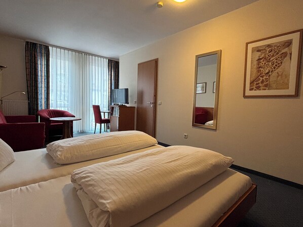 A hotel room with two beds, a desk with a chair, a television, and a large mirror. - Hotel Krone Neuenburg (Neuenburg am Rhein)