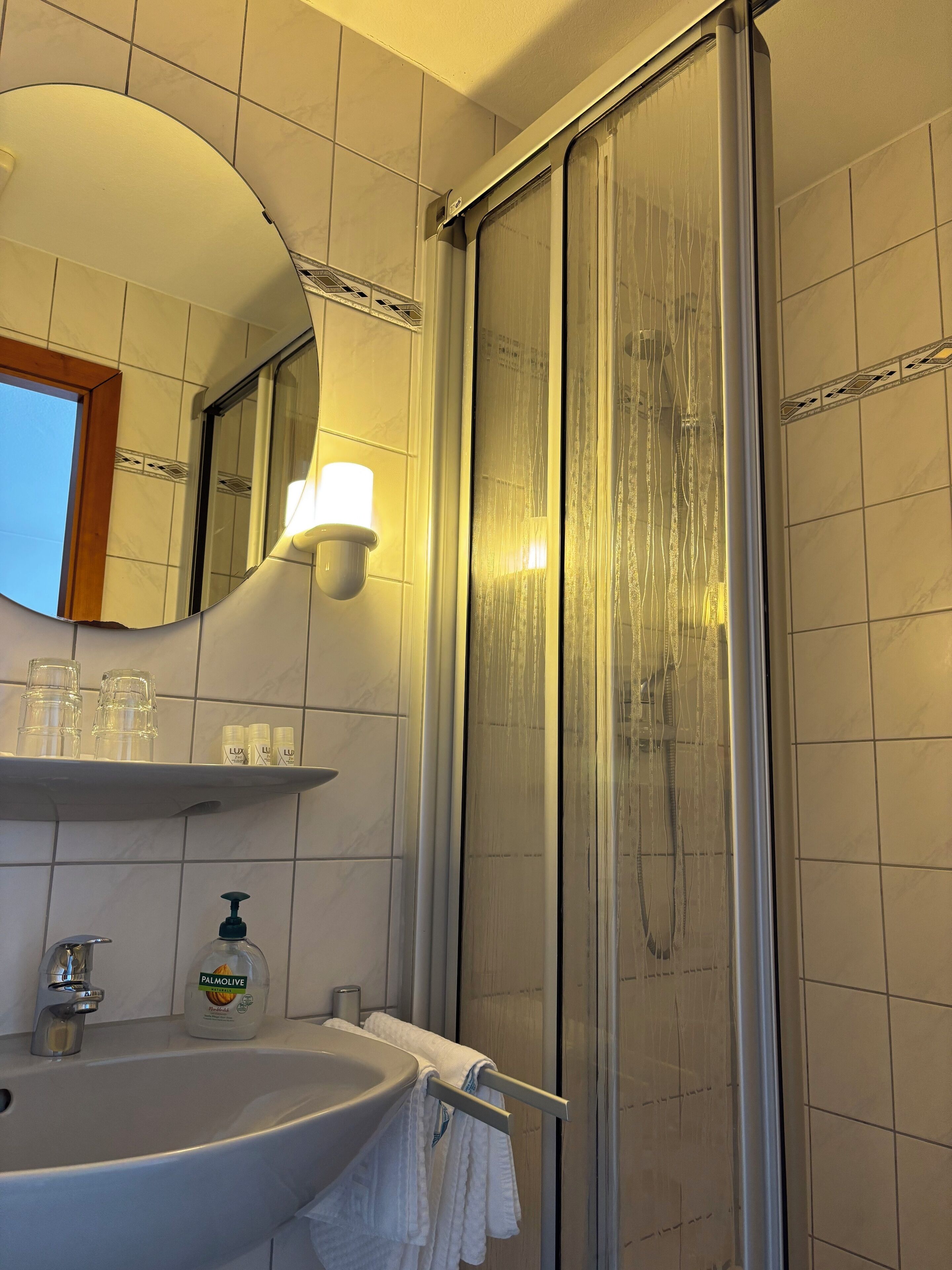 A bathroom with a sink, mirror, shower, and shelves with toiletries.
