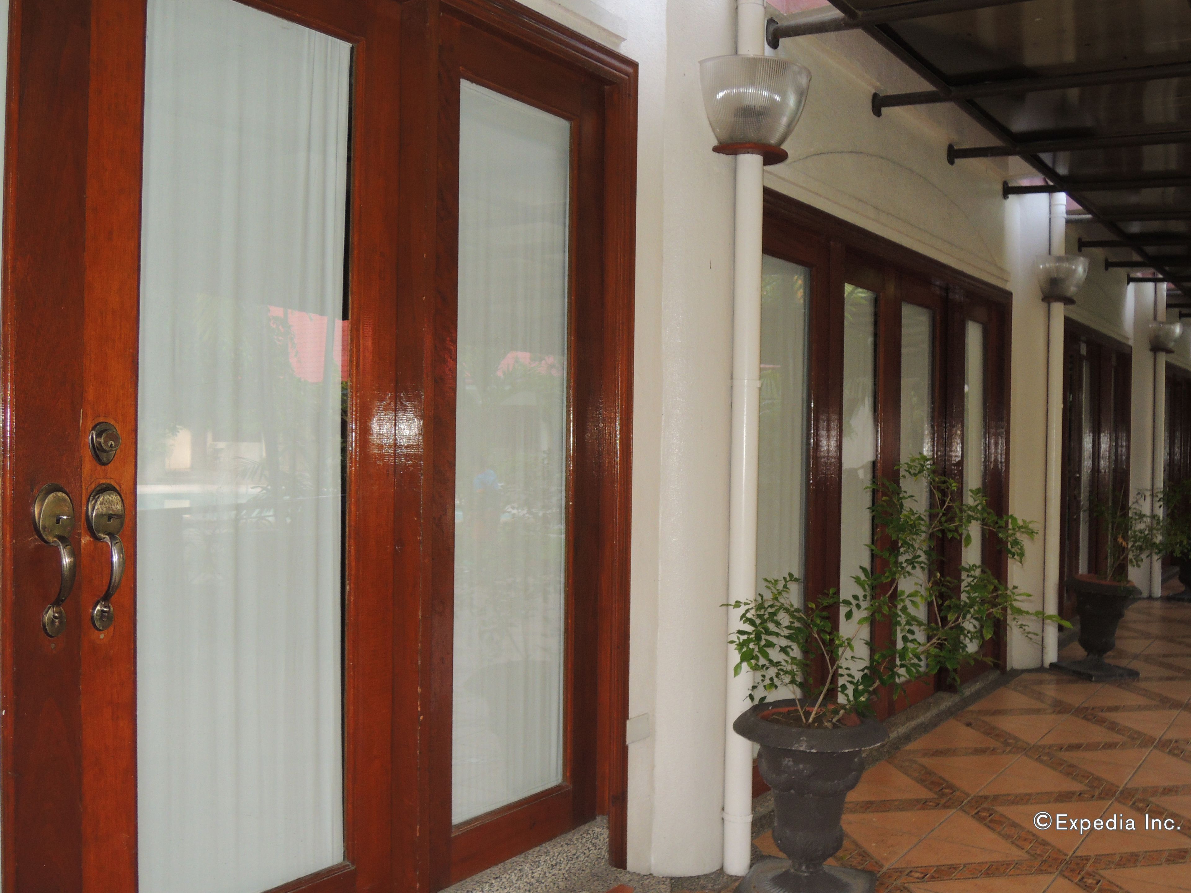 A corridor with wooden doors, white columns, and potted plants.