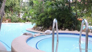 Una piscina de borde curvo, rodeada de rocas y abundante vegetación.