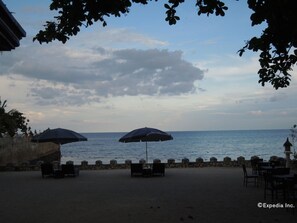 A seaside patio with two umbrellas, stone walls, and tables.