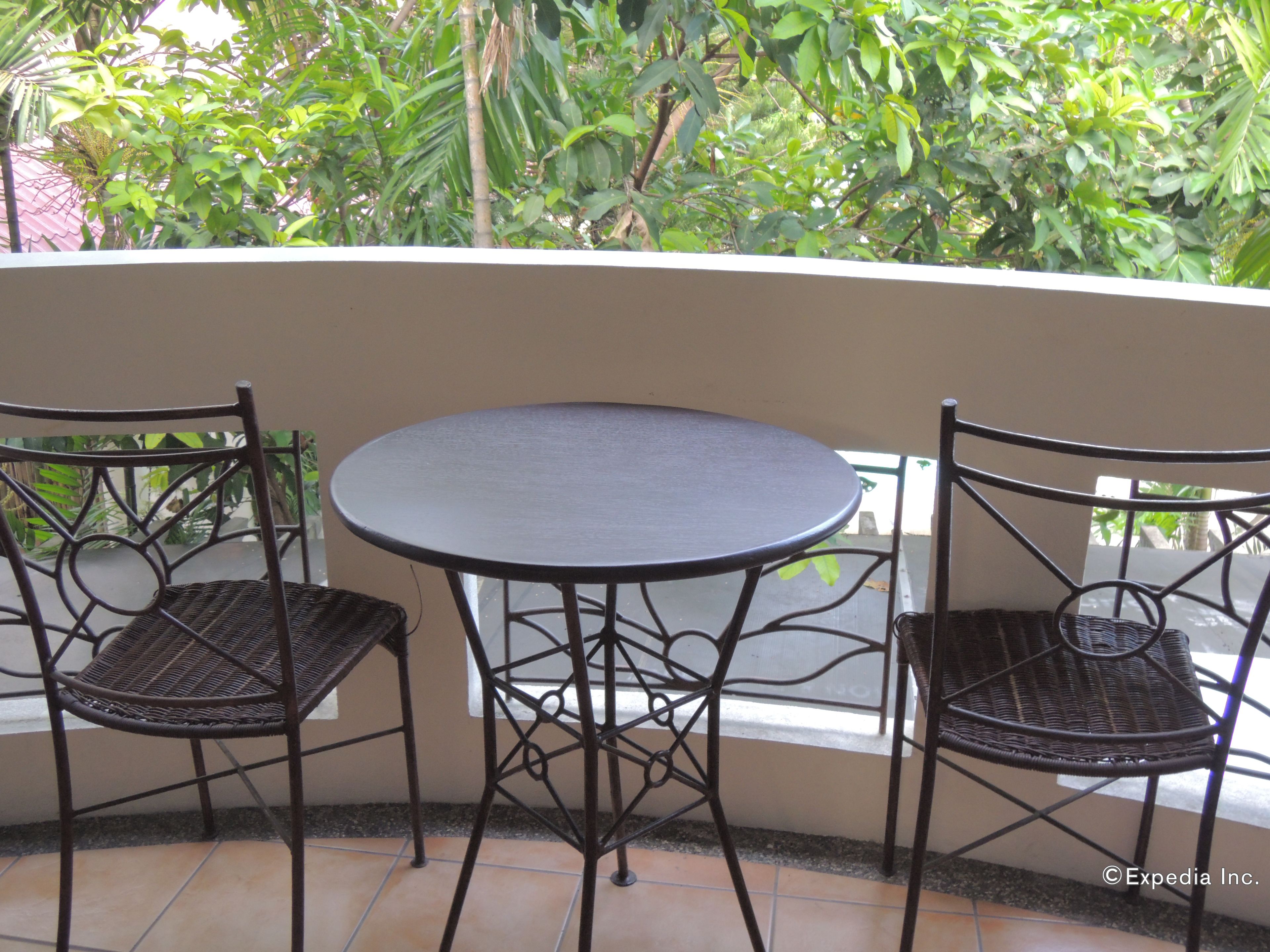 Een klein balkon buiten met een ronde tafel en twee rieten stoelen.
