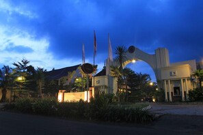 A building with a large archway and multiple flags, surrounded by palm trees and well-lit pathways. - The Gambir Anom Hotel Resort & Convention (Ngemplak)